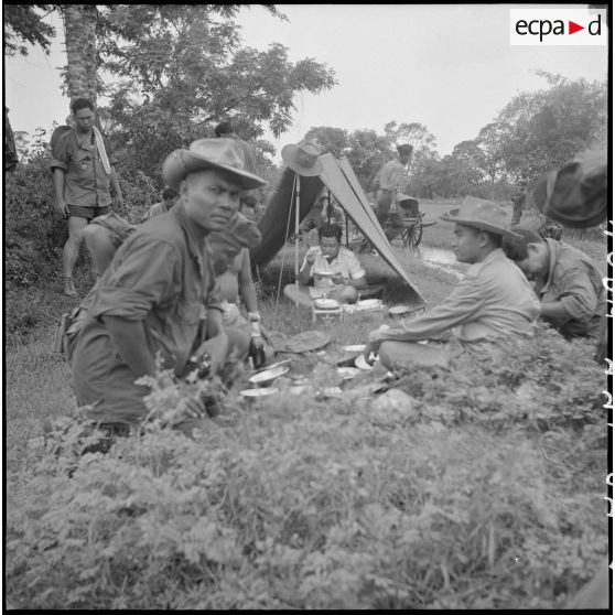 M. Norodom Sihanouk en train de manger à l'entrée de sa tente. [description provisoire]