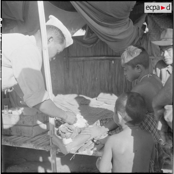 Soins prodigués à  petite fille, accompagnée de son frère et à un chasseur cambodgien  par l'infirmier du poste. [description provisoire]
