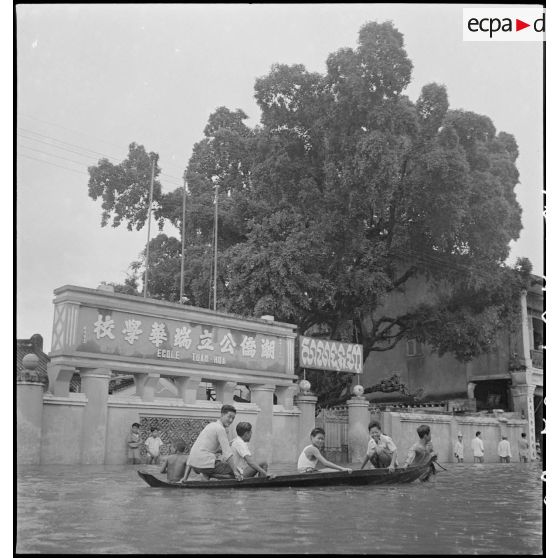 Cambodgiens circulant sur une pirogue devant l'école Tuan-Hoa, à Phnom Penh, après le passage d'un typhon. [description provisoire]
