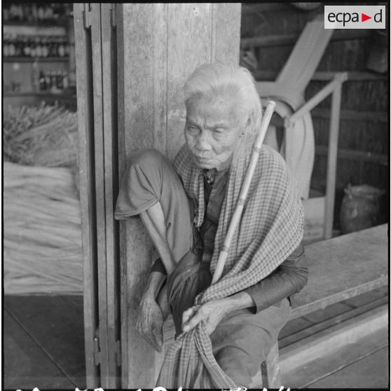 Femme cambodgienne drapée dans son ""Kra ma"", le foulard traditionel khmer (à carreaux rouges et blancs) aux utilisations multiples (foulard, pagne, ceinture, panier, turban, pansement de fortune, natte etc.) et dont le port reste très répandu parmi les soldats de l'ARK (Armée Royale Khmère). [description provisoire]