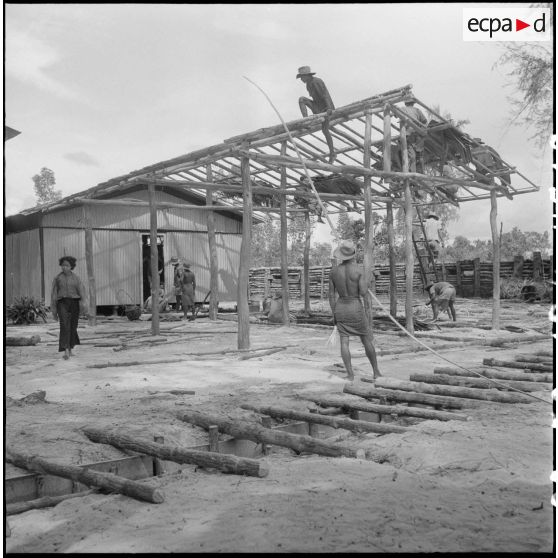 A cent kilomètres au nord de Réam, face à la pointe Nord de l'île de Koh-Kong et près de l'îlot Cône, le poste de Lem Dam est en cours de construction. Le bâtiment dont la charpente est en train d'être installée servira de hall d'entrée et de popote. En arrière plan, la baraque préfabriquée abrite le poste de commandement. [description provisoire]