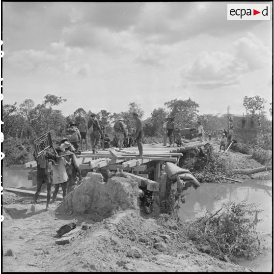Une équipe s'active à la reconstruction d'un pont brûlé par le Viêt-minh quelques jours auparavant. [description provisoire]