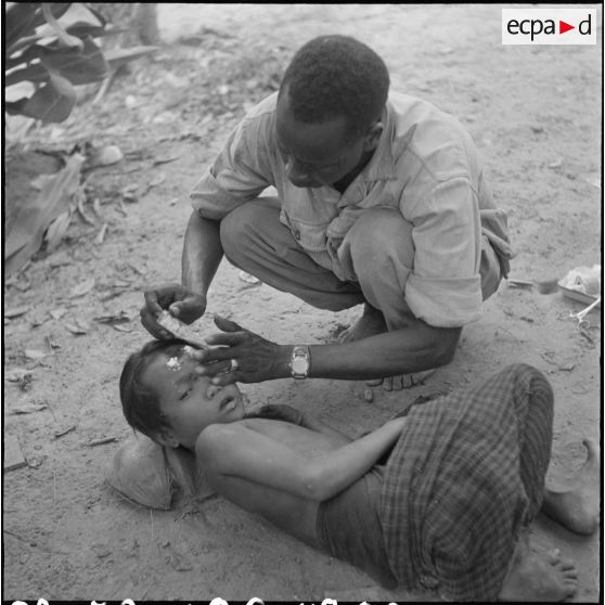 A la pagode de Wa Chot, un infirmier du 2/6e RIC (2e bataillon du 6e Régiment d'Infanterie Coloniale) donne ses soins à une fillette cambodgienne. [description provisoire]