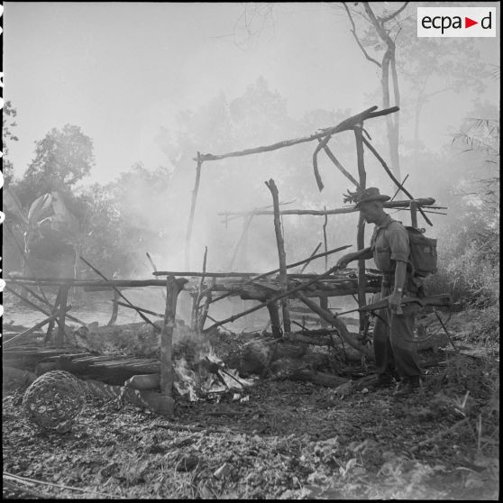 Muni d'une carabine US M1, un cadre du 2/6e RIC (2e Bataillon du 6e Régiment d'Infanterie Coloniale) contemple les ravages du feu sur le bamboux lors de la destruction d'un camp Viêt-minh ayant servit d'abri provisoire à la colonne. [description provisoire]