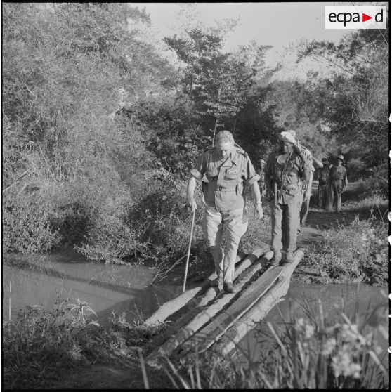 18 Le général Girot de Langlade, franchit un stung (rivière) sur un pont de fortune, suivi d'un soldat cambodgien. [description provisoire]