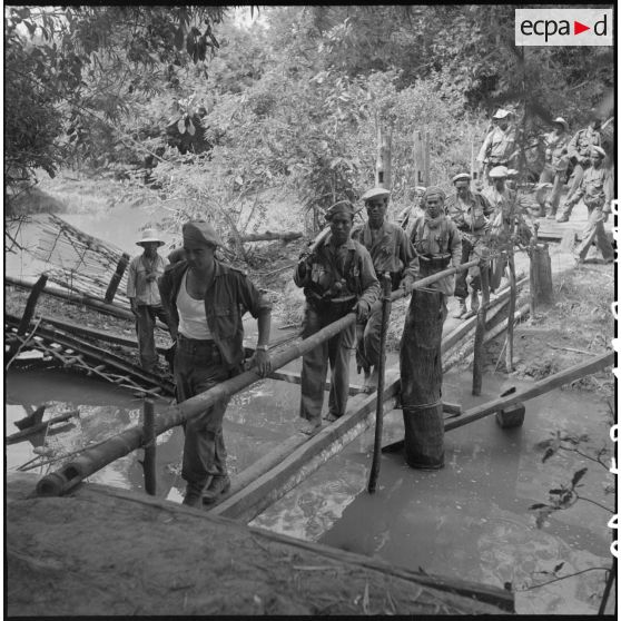 9 L'adjudant-chef Fournier,à la tête de la colonne, traverse une rivière sur un pont de fortune. [description provisoire]