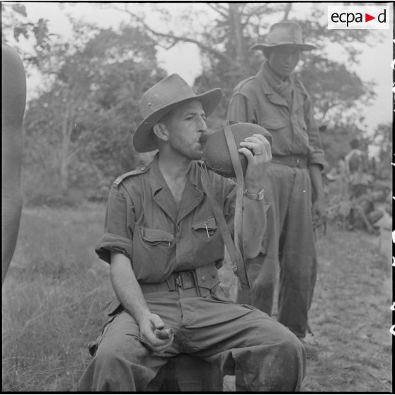 24 Le médecin-capitaine Lapeyre, assis, se désaltère en buvant l'eau d'une gourde ; à ses côtés, un militaire debout. [description provisoire]