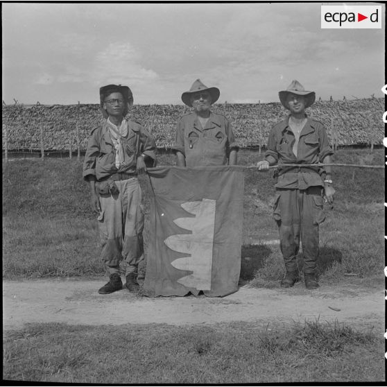 26 Le capitaine Roehrich, commandant le 3/RMC entouré de 2 militaires cambodgiens tient un drapeau KI (Khmer Issarak). [description provisoire]