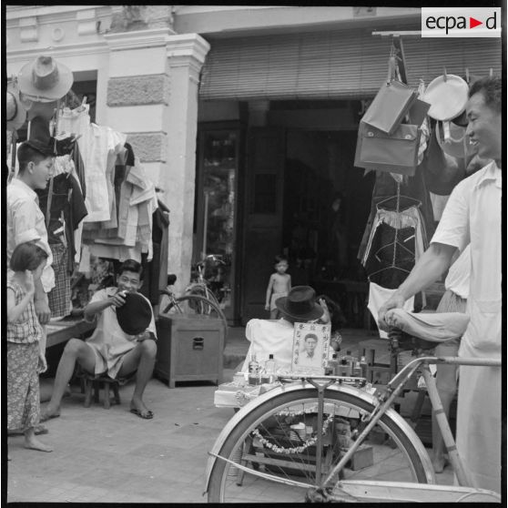 33 à 34 Dentiste ambulant effectuant des soins sur une patiente, dans la rue près d'un présentoir de bérets. [description provisoire]