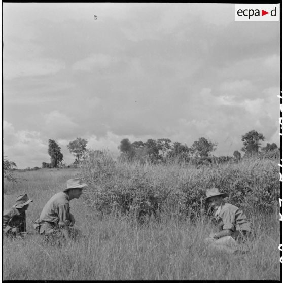 34 Trois militaires, agenouillés dans les herbes, procèdent à la destruction de mines récupérées. [description provisoire]