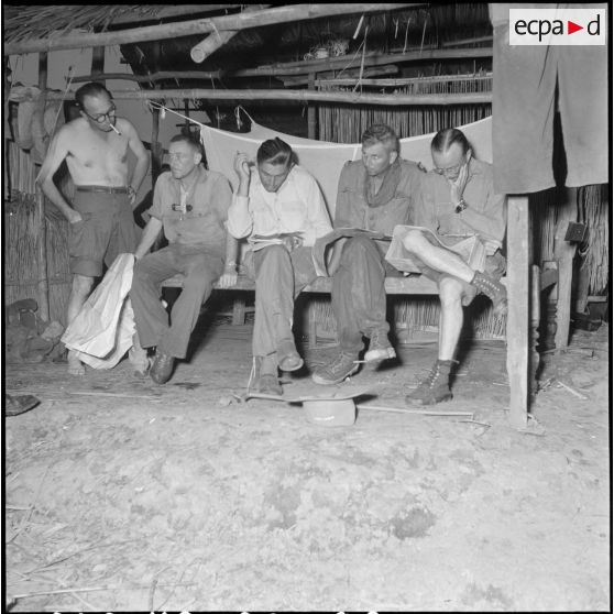 Briefing des commandants de compagnie du 2 bataillon du 43e régiment d'infanterie coloniale au cours de l'opération Tourbillon VII pendant que sèche, au premier-plan, le pantalon du reporter Coutard. [description provisoire]