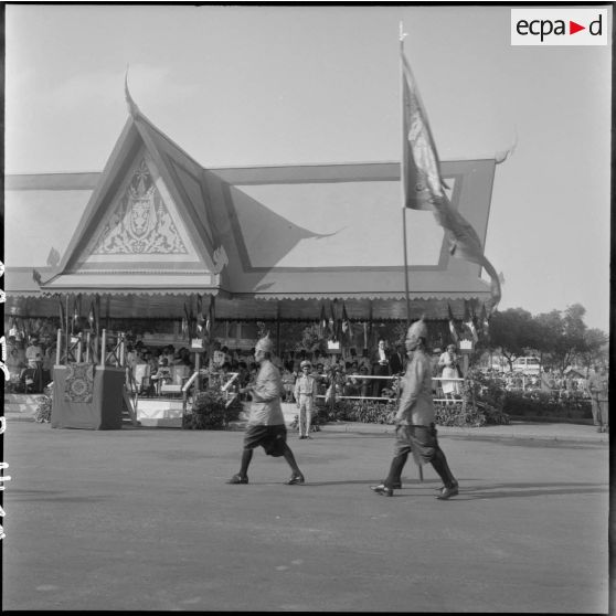 Couronnement du roi Suramarit et de la reine Kossamak du Cambodge à Phnom Penh : le groupe des serviteurs du palais, portant un étendard et précédant le cortège royal, passe devant la tribune officielle. [description provisoire]
