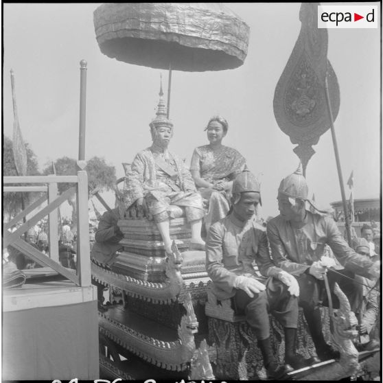 Le roi Suramarit et la reine Kossamak du Cambodge assis sur le char royal et abrités par une ombrelle lors des cérémonies de couronnement. [description provisoire]
