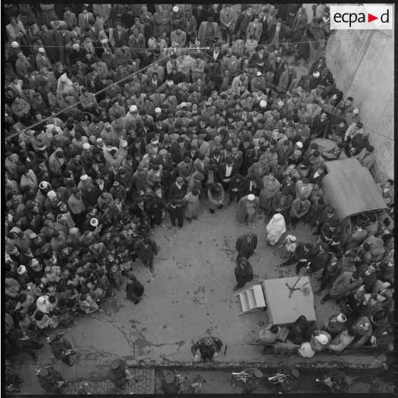 Plusieurs centaines de personnes entourent le podium où des orateurs prennent tour à tour la parole.