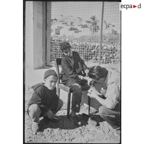 Ecolier se faisant soigner le pied par son instituteur.