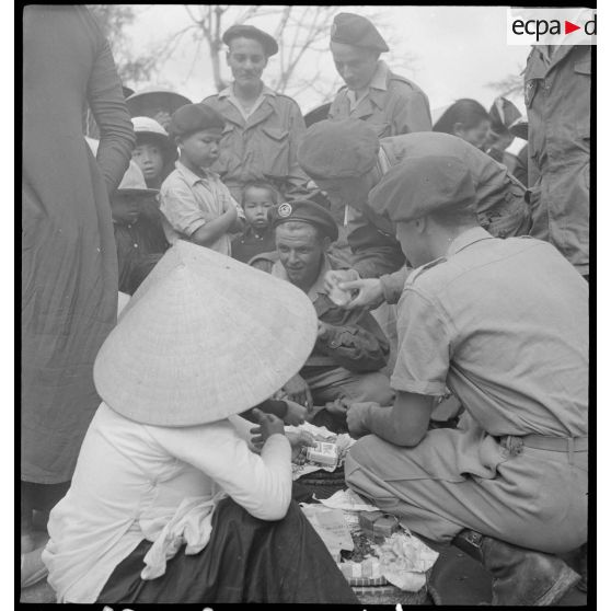 Des hommes du 6e bataillon colonial de commandos parachutistes dans une rue de Hué, auprès de marchands de rue.