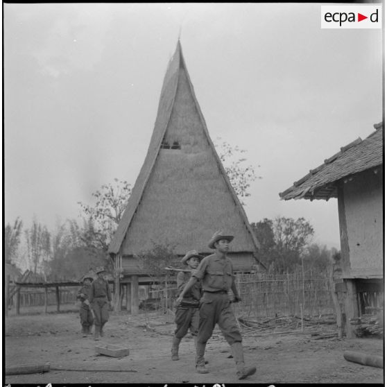 Au retour d'une patrouille, des soldats vietnamiens traversent un village montagnard de la région de Kon Tum où se dresse une maison communale.