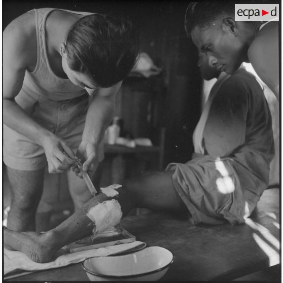 Un chasseur laotien blessé est soigné par le médecin-lieutenant Guiraud à l'intérieur d'une paillote, au cours de l'opération Frimaire dans la province de Xieng Khouang.