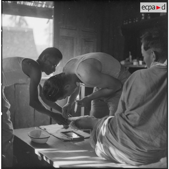 Un chasseur laotien blessé est soigné par le médecin-lieutenant Guiraud à l'intérieur d'une paillote, au cours de l'opération Frimaire dans la province de Xieng Khouang.