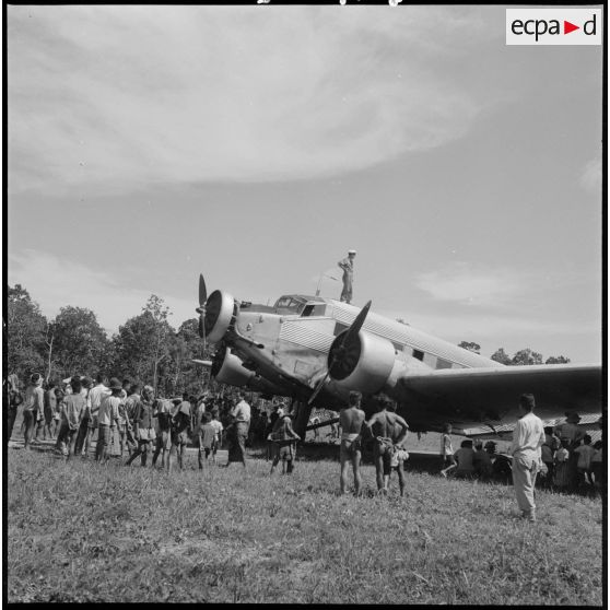 Des habitant d'Attapeu sont rassemblés autour d'un avion posé sur un terrain débroussaillé par la garnison.
