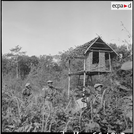 Une colonne de chasseurs 2e bataillon de chasseurs laotiens (2e BCL) passe près d'une paillotte de garde dans un rays.