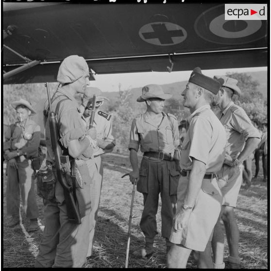 Des officiers du 2e bataillon de chasseurs laotiens (2e BCL) s'entretiennent devant un avion sanitaire venu chercher des malades.