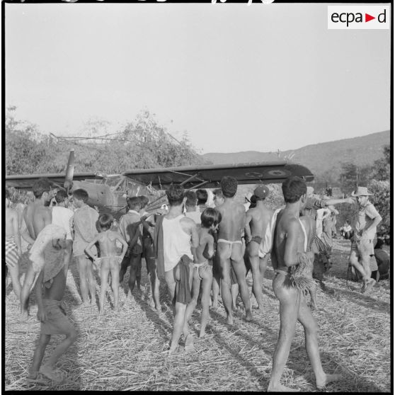 Des villageois Kha attroupés autour d'un avion Morane Saulnier sanitaire.