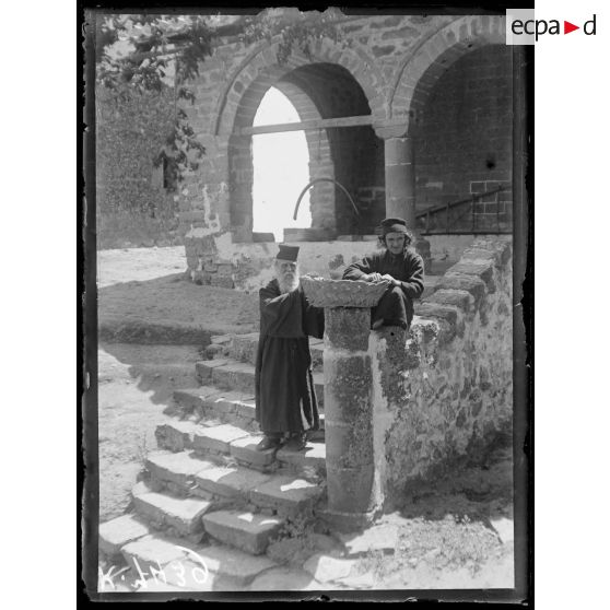 Les Météores (Thessalie). Monastère d'Hagios Stéphanos. Deux moines. Sous les arcades, un arc sert de cloche. [légende d'origine]