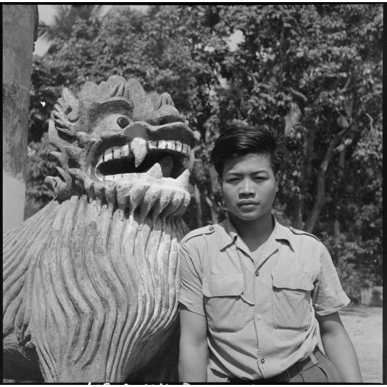 Jeune homme lao posant devant une statue de lion au Vat Sirimoungkhoun Sayaram, à Luang Prabang.