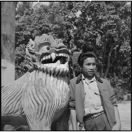 Jeune homme lao posant devant une statue de lion au Vat Sirimoungkhoun Sayaram, à Luang Prabang.