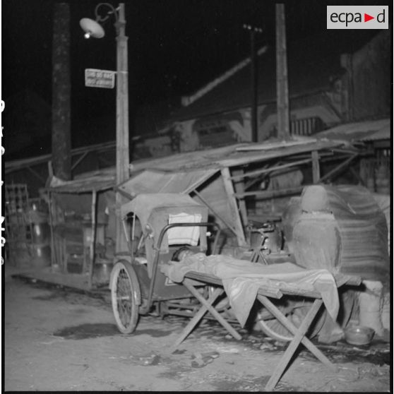 Vietnamien dormant sur une planche près d'un pousse-pousse dans une rue de Saigon.