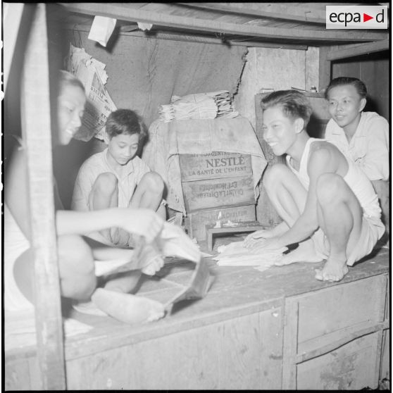 Jeunes garçons pliant des journaux dans une échoppe de rue à Saigon.
