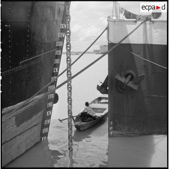 Dans le port de Saigon, des vietnamiennes à bord d'une barque entourée d'imposants navires.