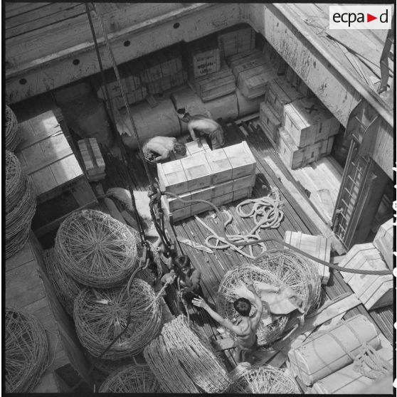Déchargement de matériel (caisses et rouleaux de barbelé) transporté dans un navire au port de Saigon.