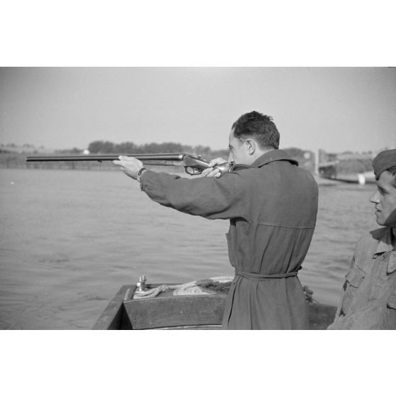 Depuis une embarcation, un officier roumain du Grupul 9 tire au fusil de chasse.