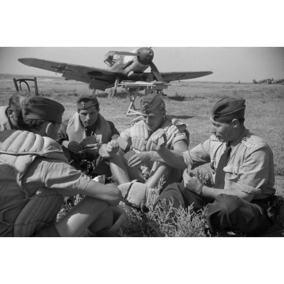 Pilotes roumains et allemands jouant aux cartes, derrière eux un chasseur Messerschmitt Bf-109.