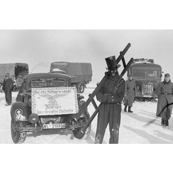 Déguisé en ramoneur, un membre du Sturzkampfgeschwader 2 Immelmann accompagne une affiche qui va accueillir le pilote Rudel.