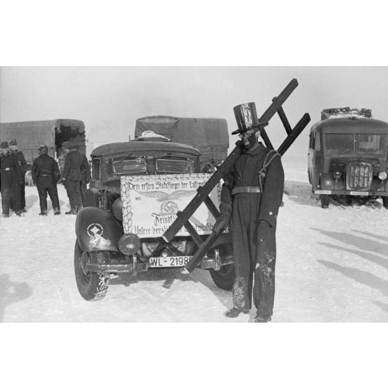 Déguisé en ramoneur, un membre du Sturzkampfgeschwader 2 Immelmann accompagne une affiche qui va accueillir le pilote Rudel.
