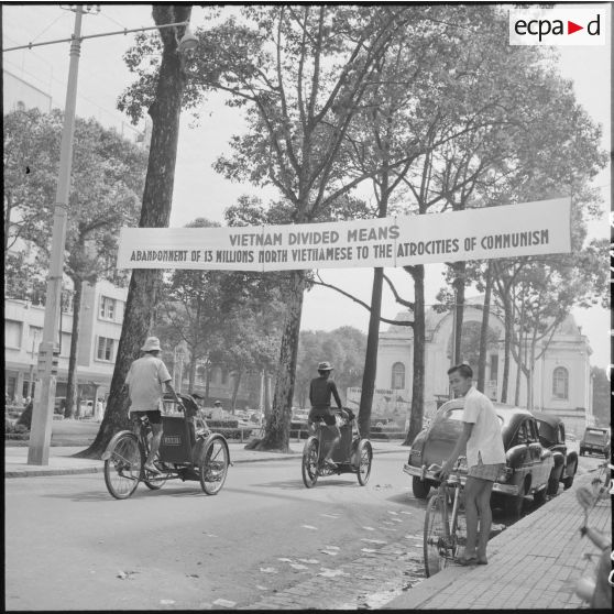 Circulation devant le théâtre de Saigon où une banderole témoigne de manifestations contre le cessez-le-feu et la partage du Vietnam.