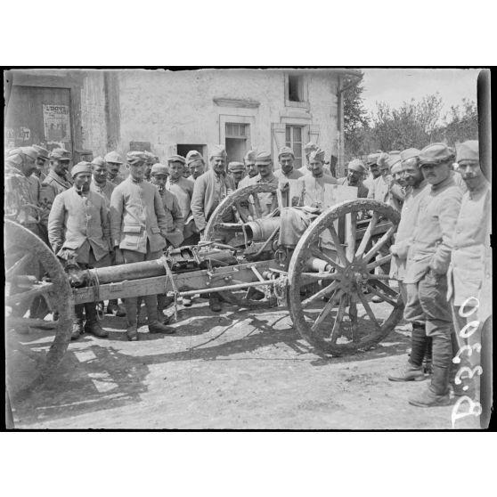 Des hommes du 64e régiment d'infanterie, dont un sapeur de cette unité,  sont assemblés autour d'un canon de 75 mm explosé.