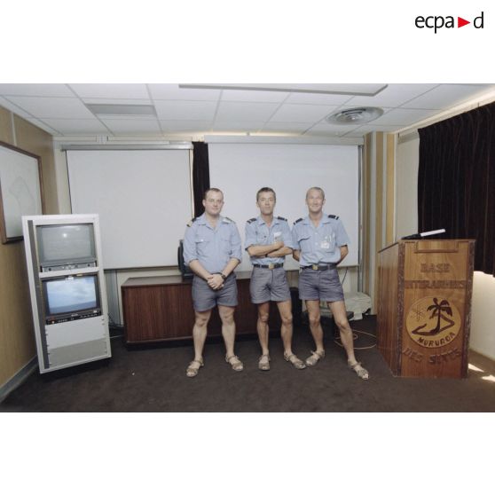 Portrait de personnel de la Marine nationale dans une salle du poste de commandement du groupement opérationnel des essais nucléaires (GOEN) pendant le tir nucléaire Aepytos du 27 octobre 1995. Un comptoir porte l'inscription et l'insigne de la base interarmées (BIA) des sites de Moruroa.