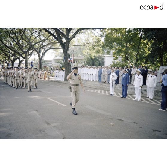 Défilé des troupes devant Charles Hernu, ministre de la Défense, lors d'une cérémonie militaire à Papeete, accompagné de Paul Noirot-Cosson, haut-commissaire de Polynésie française, du contre-amiral Jacques Choupin, commandant le Centre d'expérimentations du Pacifique (CEP), et du contre-amiral René Hugues, chef du cabinet militaire.