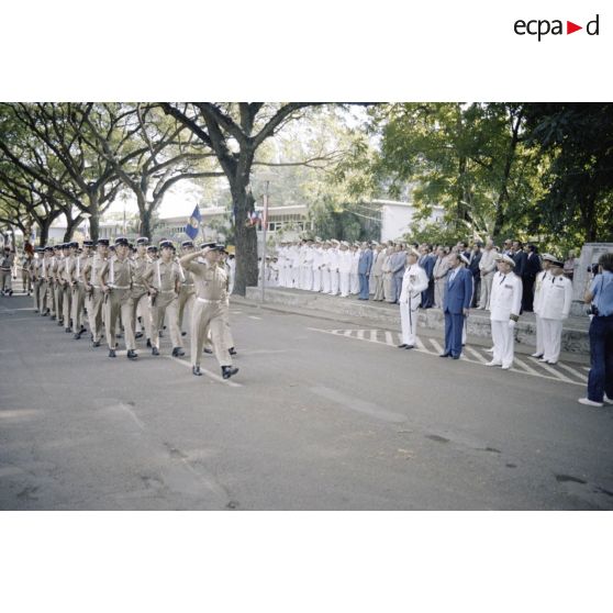 Défilé des troupes devant Charles Hernu, ministre de la Défense, lors d'une cérémonie militaire à Papeete, accompagné de Paul Noirot-Cosson, haut-commissaire de Polynésie française, du contre-amiral Jacques Choupin, commandant le Centre d'expérimentations du Pacifique (CEP), et du contre-amiral René Hugues, chef du cabinet militaire.