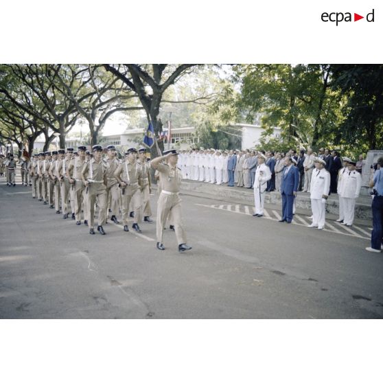 Défilé des troupes devant Charles Hernu, ministre de la Défense, lors d'une cérémonie militaire à Papeete, accompagné de Paul Noirot-Cosson, haut-commissaire de Polynésie française, du contre-amiral Jacques Choupin, commandant le Centre d'expérimentations du Pacifique (CEP), et du contre-amiral René Hugues, chef du cabinet militaire.