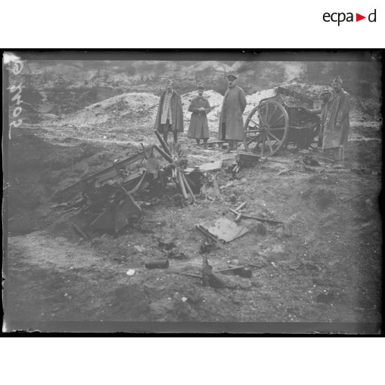 [Des soldats sont réunis autour de la carcasse d'un véhicule, au milieu d'un terrain dévasté.]