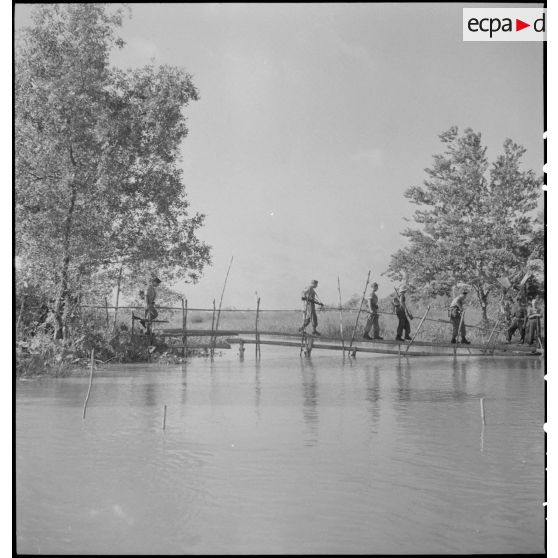 Militaires français traversant un pont, au-dessus d'une rivière.