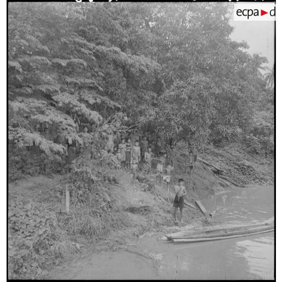 Groupe de laotiens posant sur une rive à la lisière d'une forêt d'arbres tropicaux.