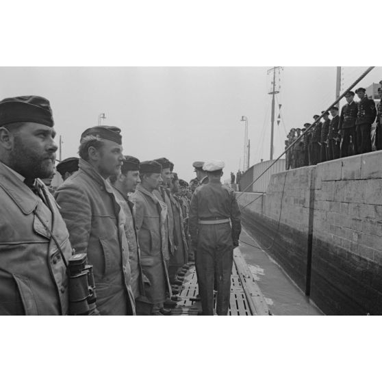 Lors de son retour de croisière à Saint-Nazaire, un officier de la 7.Unterseebootsflottille passe en revue l'équipage du sous-marin U-552 en compagnie de son commandant le lieutenant (Leutnant zur See) Erich Topp.