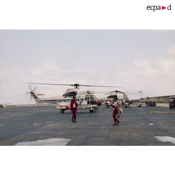 Des plongeurs rejoignent deux hélicoptères Super-Puma de l'escadron de transport d'outre-mer (ETOM) 82 pour une mission d'hélitreuillage sur l'héliport de l'aéroport de l'atoll de Moruroa.