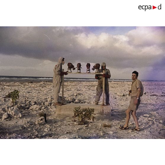 Près du poste d’enregistrement avancé (PEA) Denise, des personnels en tenue NBC relèvent des masques à gaz exposés pour étude des effets des tirs par la section technique de l’armée de terre (STAT).